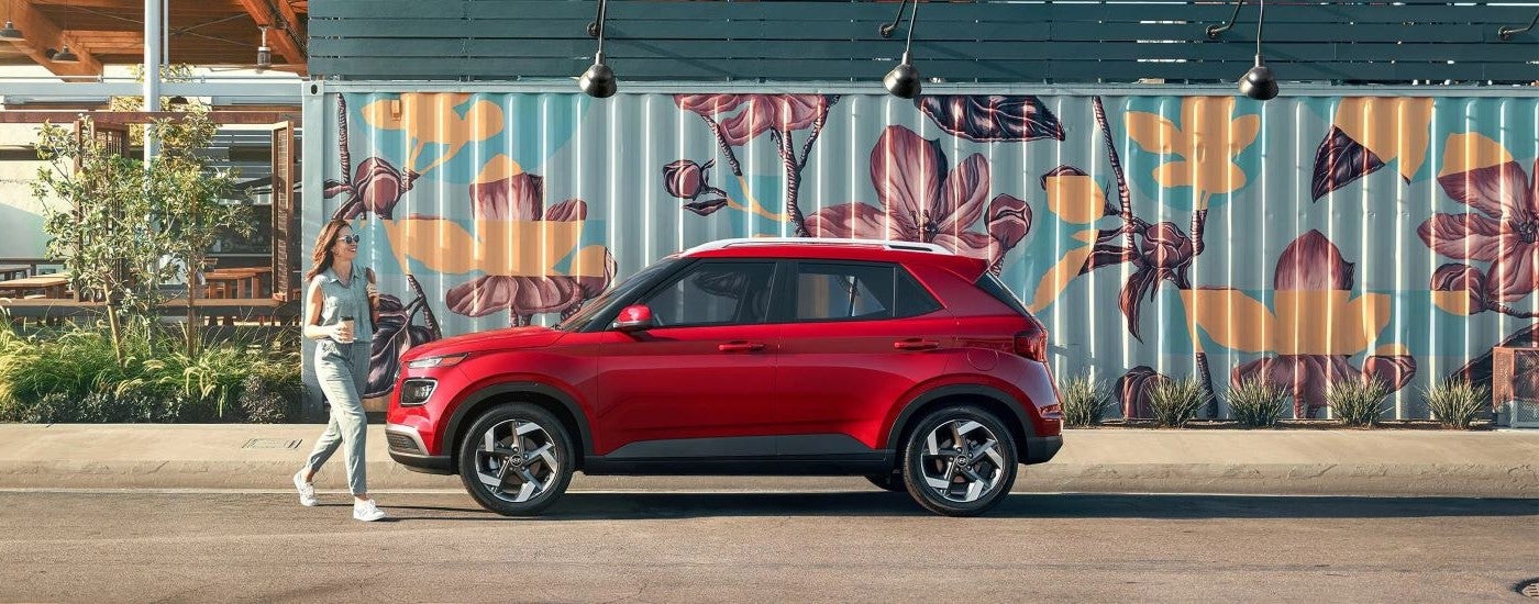 Side angle view of a red 2023 Hyundai Venue Limited parked by a Hyundai dealer near Round Lake Beach.