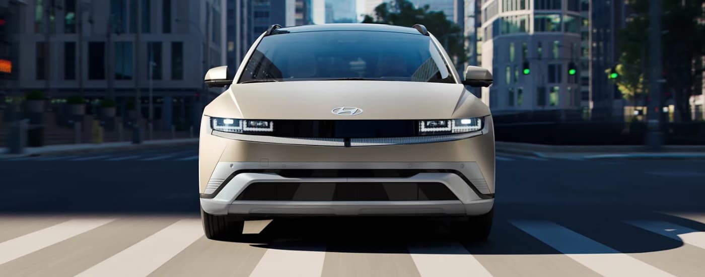 A tan 2025 Hyundai IONIQ 5 driving through a city street intersection.