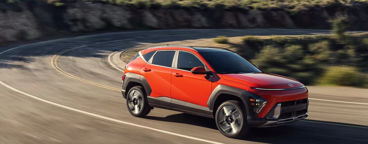 Orange 2026 Hyundai Kona driving around a bend.