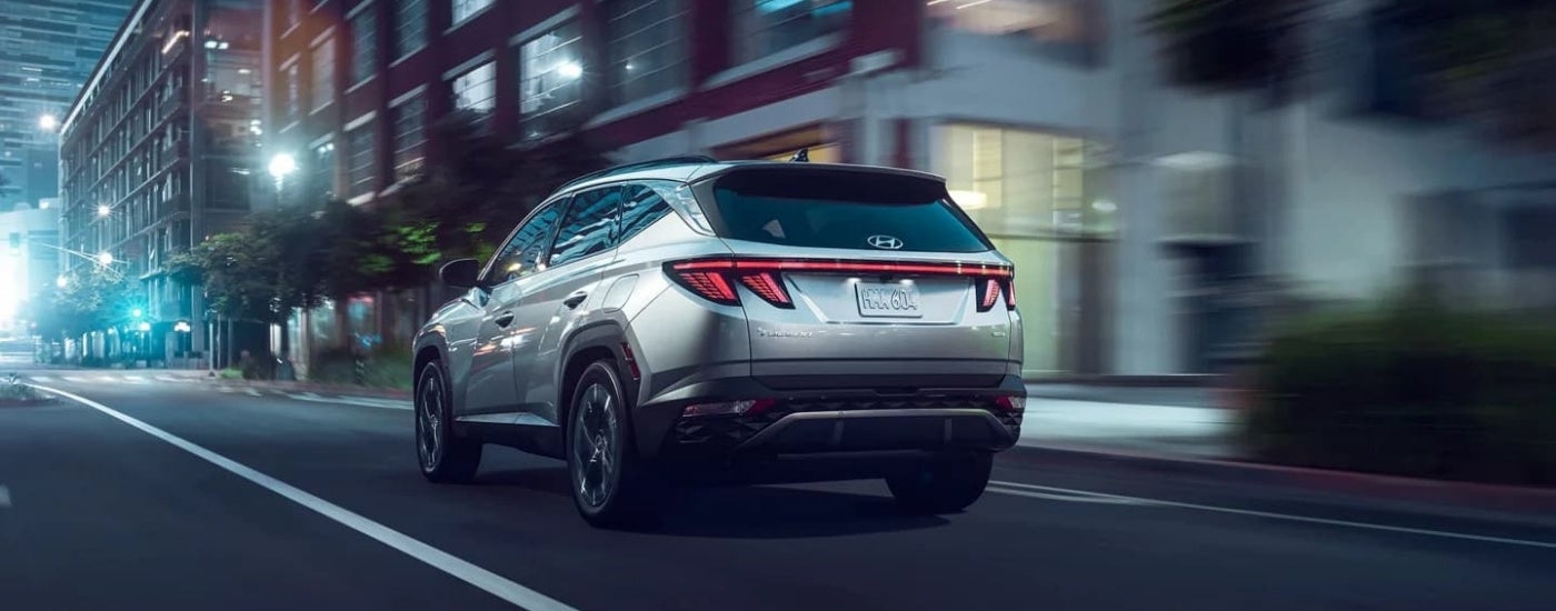 A silver 2023 Hyundai Tucson is shown from the rear driving on a city street.