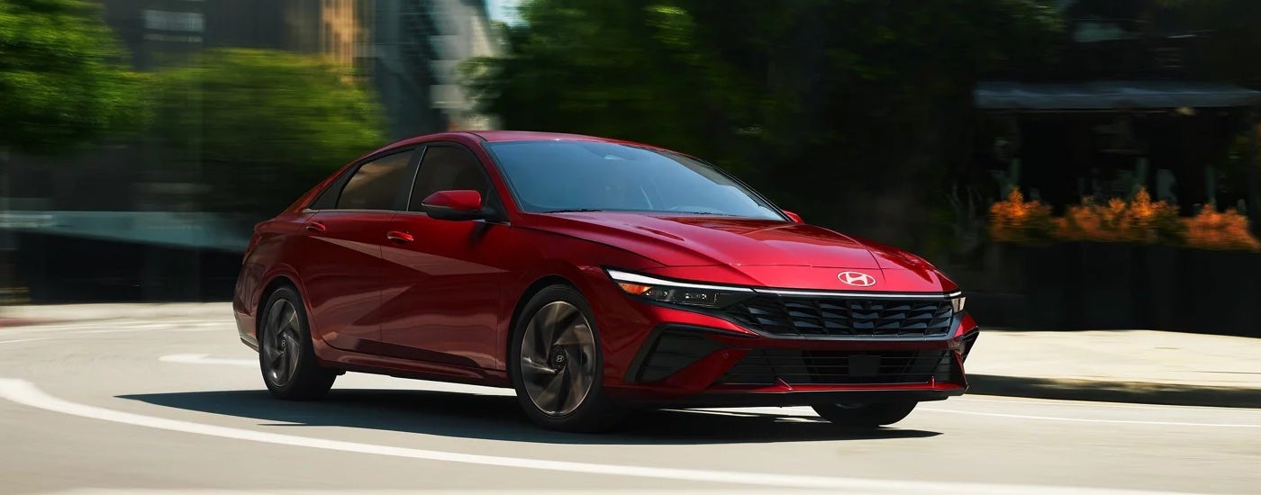 A red 2024 Hyundai Elantra Limited, a Hyundai for sale, driving on a city street.