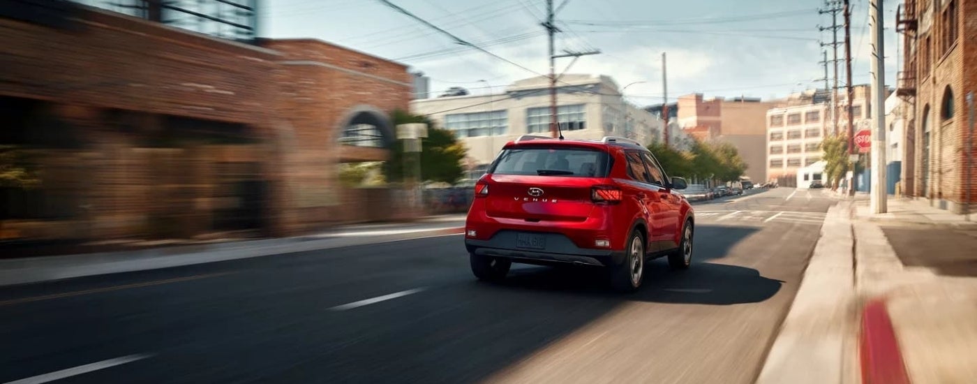 A red 2023 Hyundai Venue Limited is shown driving past a brick building.