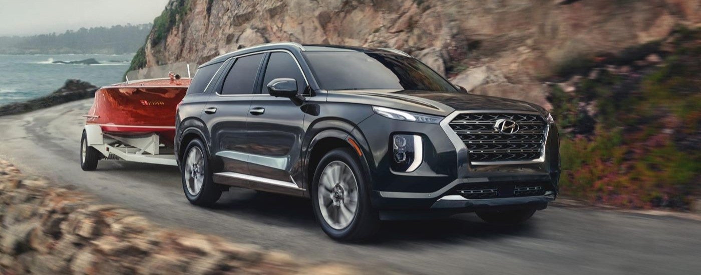 A black 2020 Hyundai Palisade towing a boat down a cliff road from a dealer with a used cars for sale.